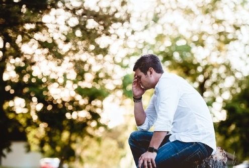 man sitting outside in thinking pose, dealing with guilt in addiction recovery